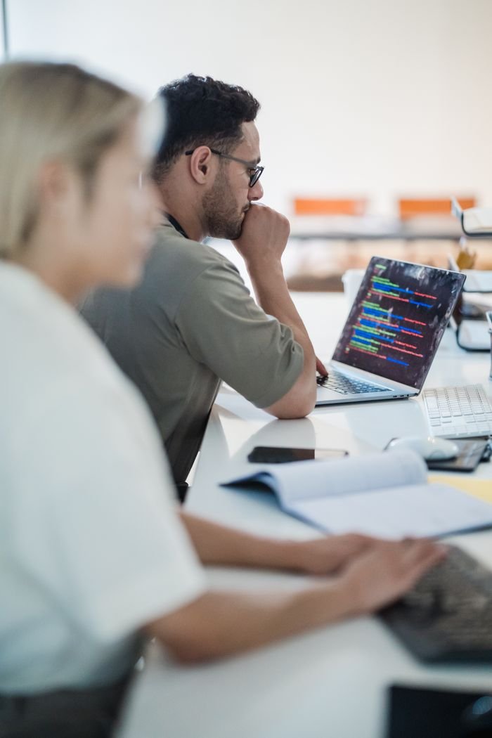Two software developers work collaboratively on a coding project in a modern office setting.